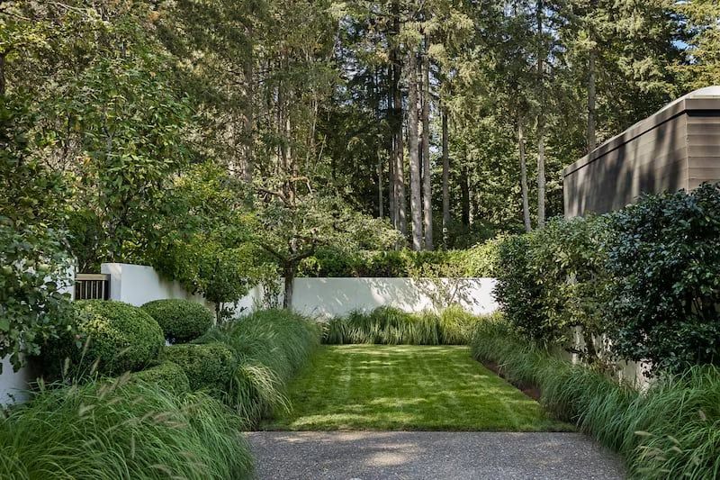 A manicured garden path lined with lush greenery, leading to a wooded backdrop.