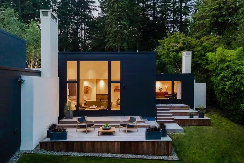 Modern home exterior with dark siding, large windows, and outdoor patio.