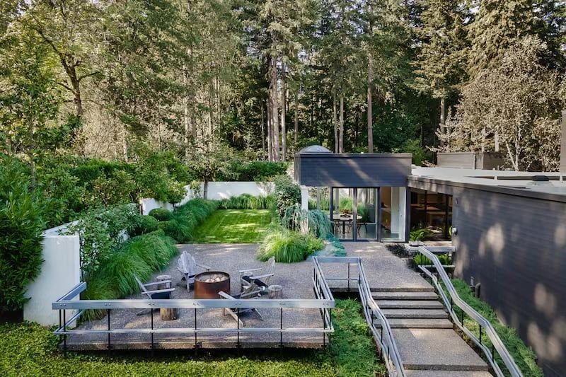 Backyard patio with fire pit, grassy area, trees, and modern building.