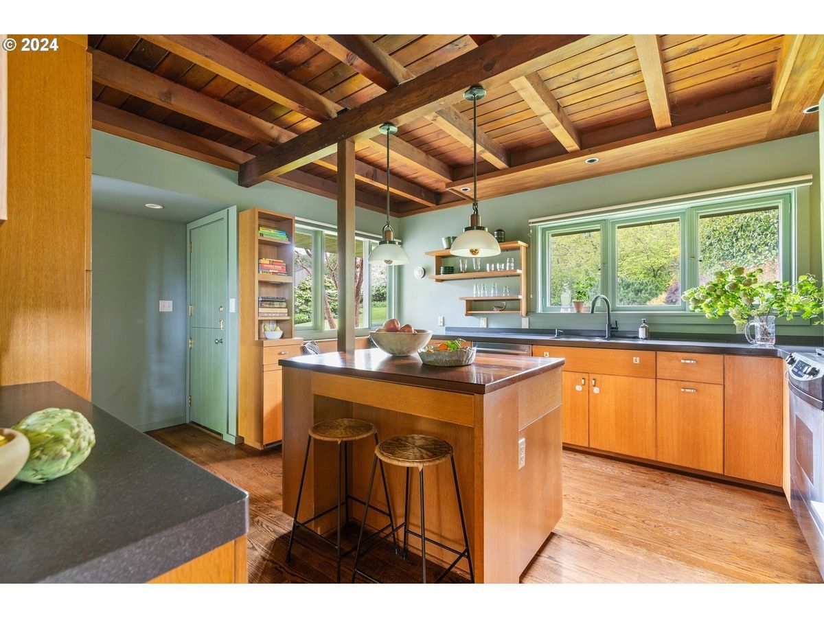 Kitchen with wood cabinets, island, and ceiling beams, featuring green walls and windows.