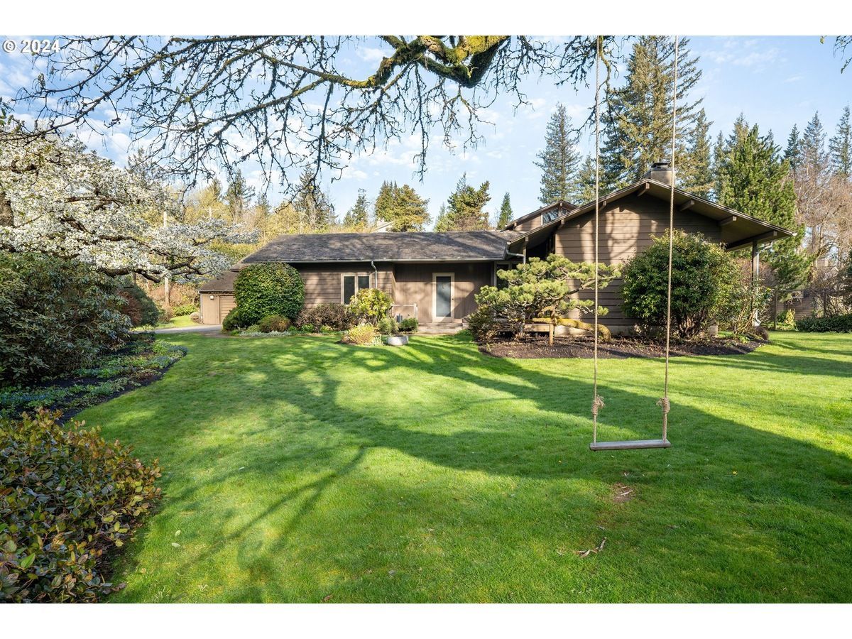 House with green lawn, swing, and trees on a sunny day.