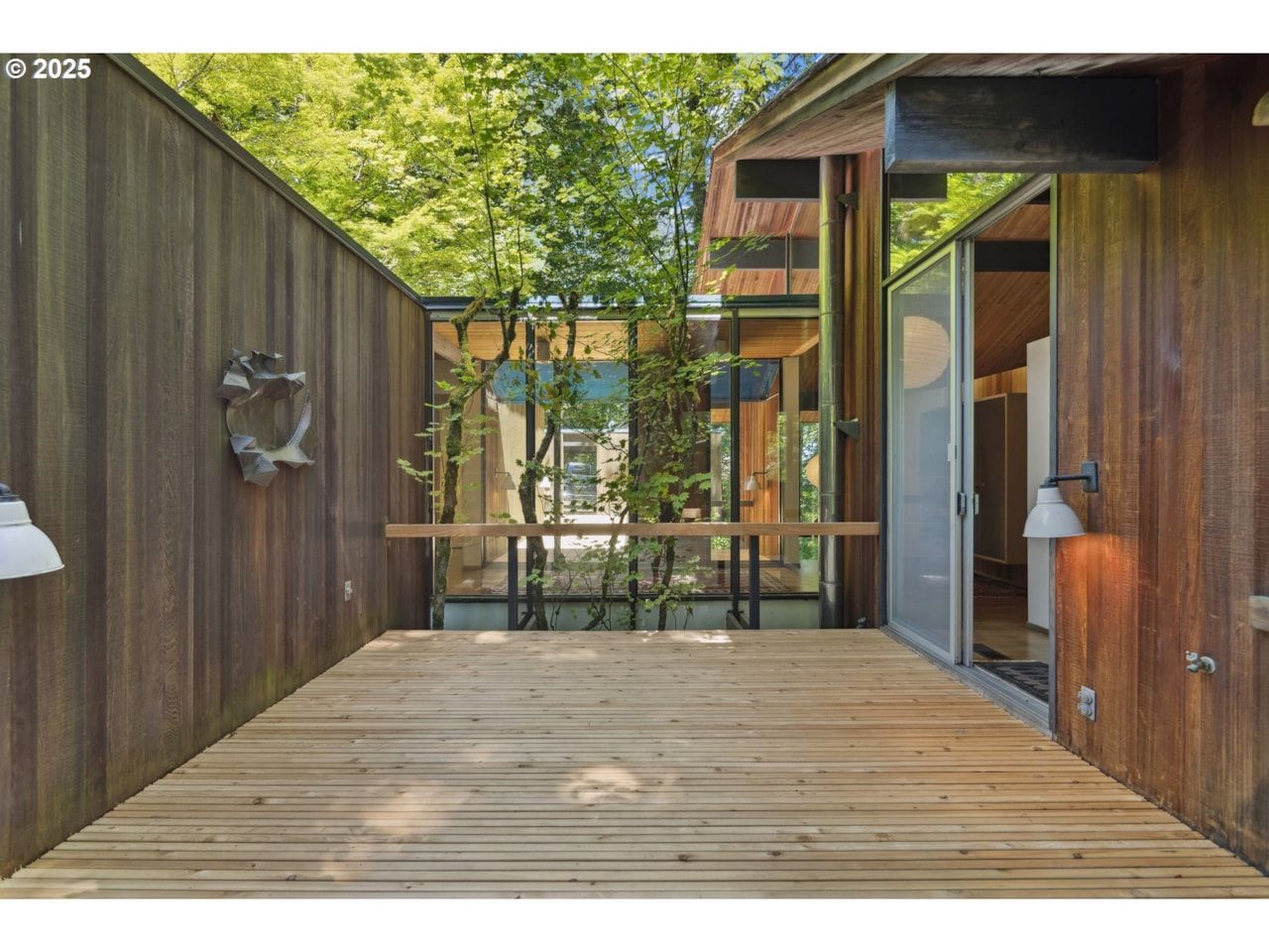 Wooden deck with wood-paneled walls and a view of a modern structure with large windows, trees visible through the structure.