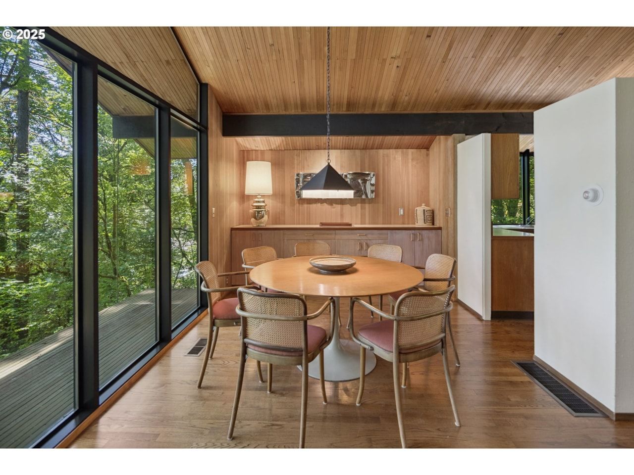 Dining room with wood paneling, large windows, and mid-century modern furniture.