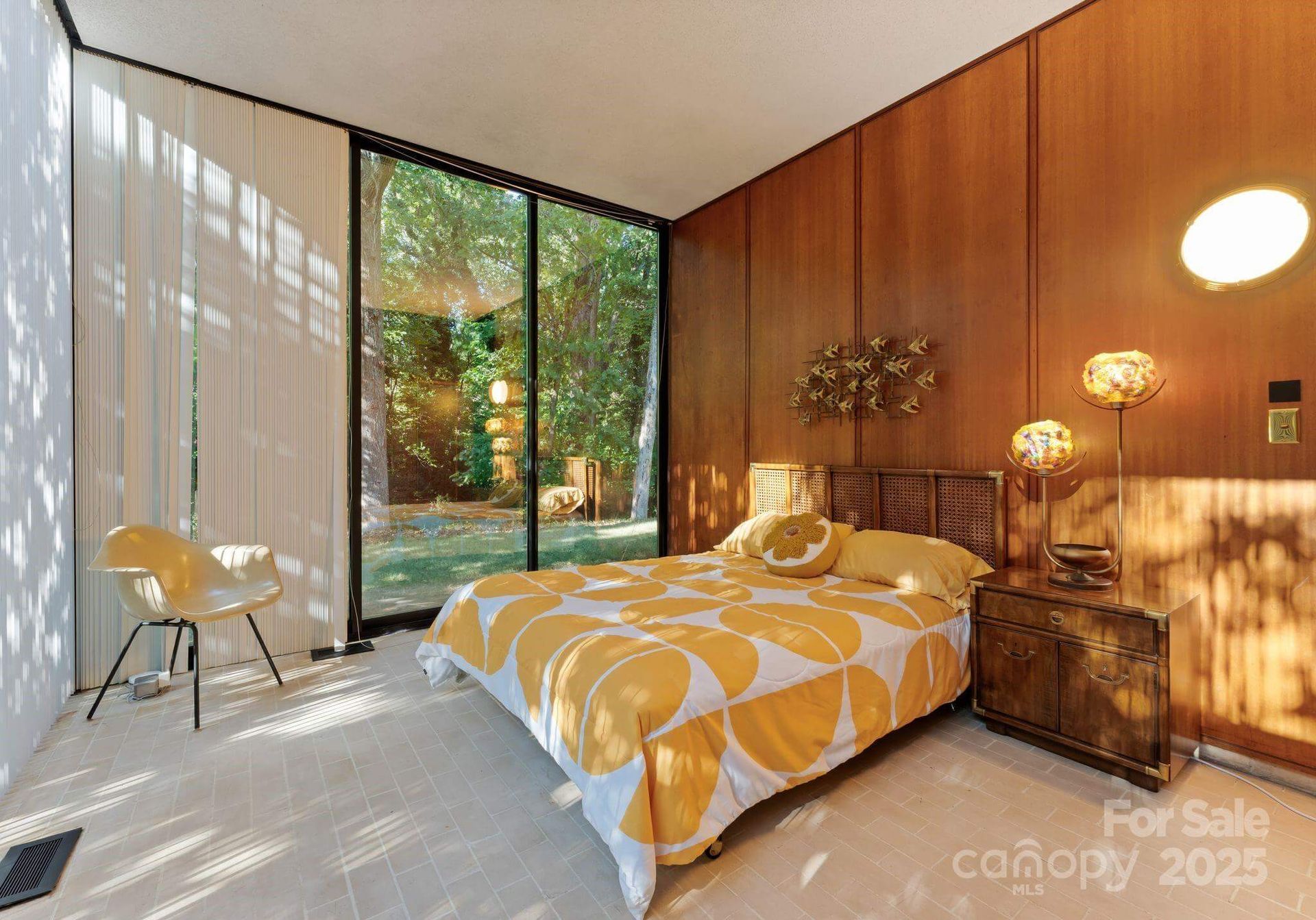 Bedroom with wood paneling, large windows, yellow bedding and chair.