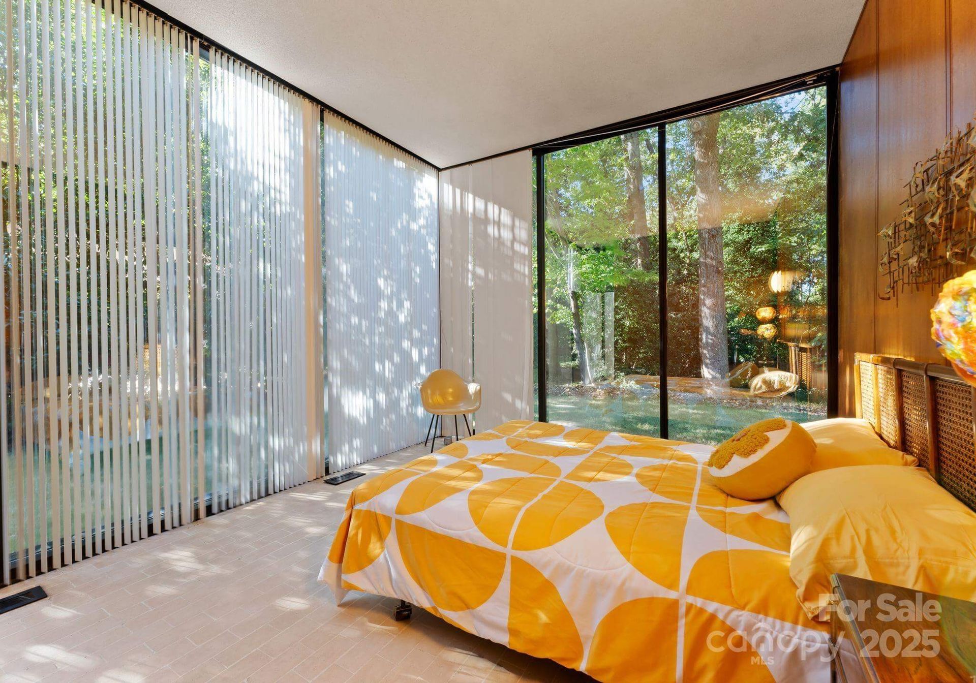 Bedroom with yellow and white bedding, sheer curtains, and large windows overlooking a yard.