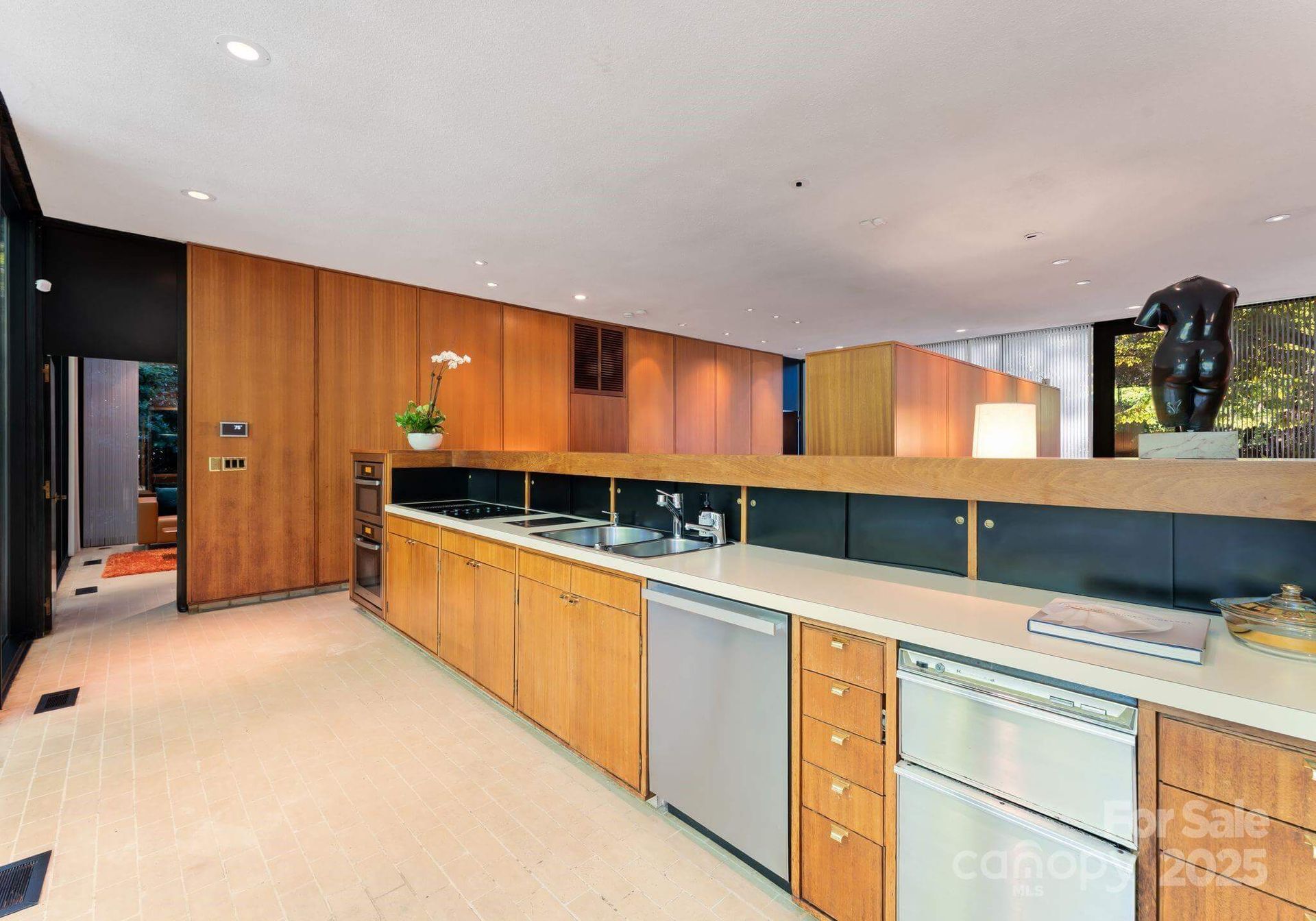 Modern kitchen with light wood cabinets, stainless steel appliances, and a sculpture.