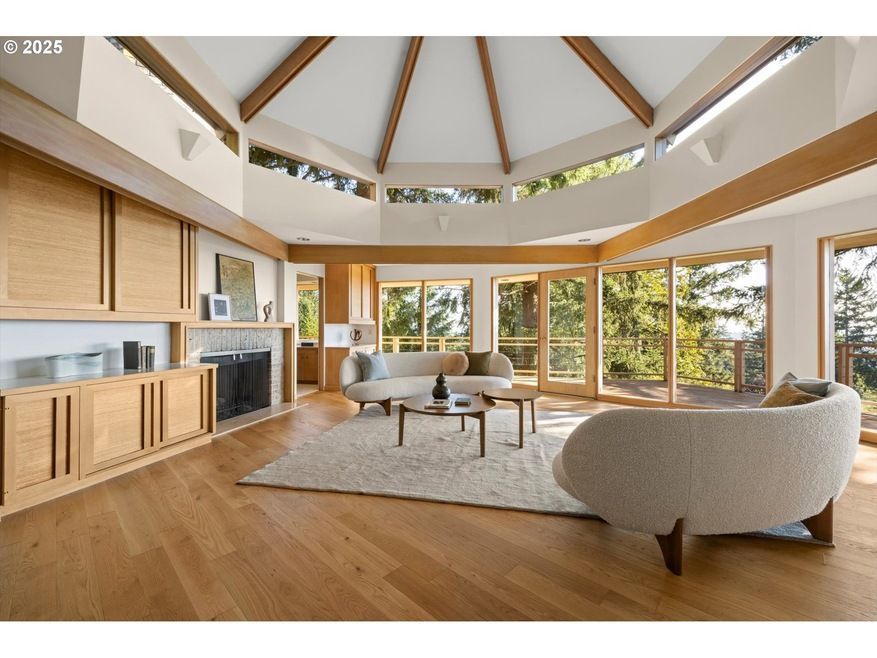 Living room with wood floors, built-in cabinets, and a domed ceiling, overlooking trees.
