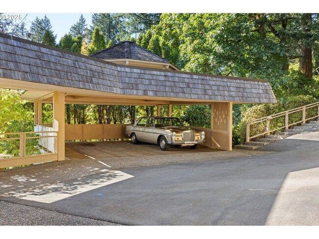 Covered parking area with a vintage silver Mercedes, wooden supports, and a shingle roof.