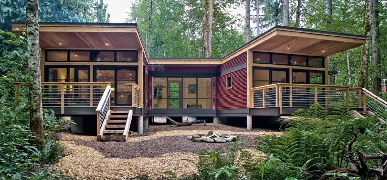 Modern cabin in a forest setting with a wooden deck and large windows.