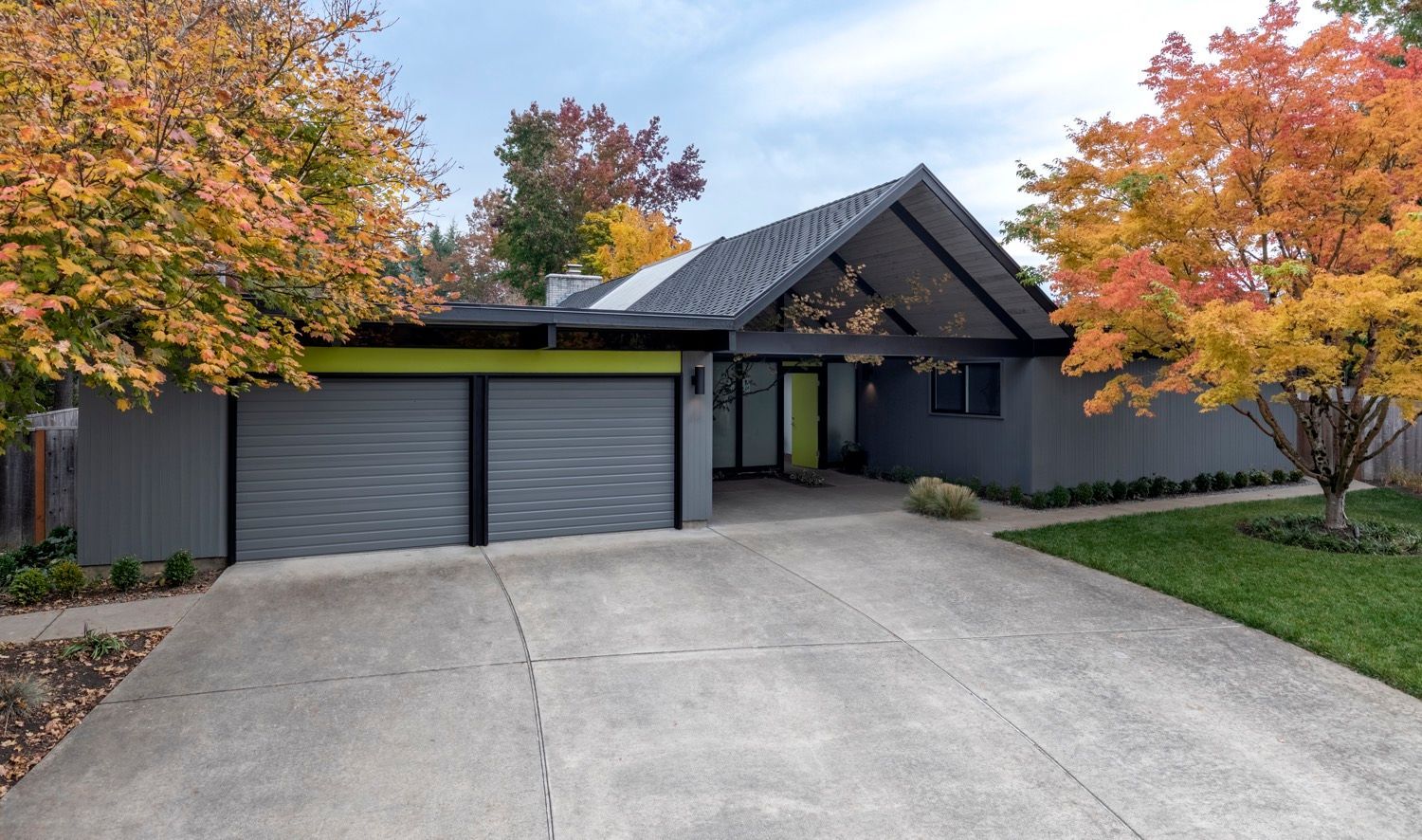 Eichler mid-century modern house with a gabled roof, two-car garage, and colorful trees in the yard.