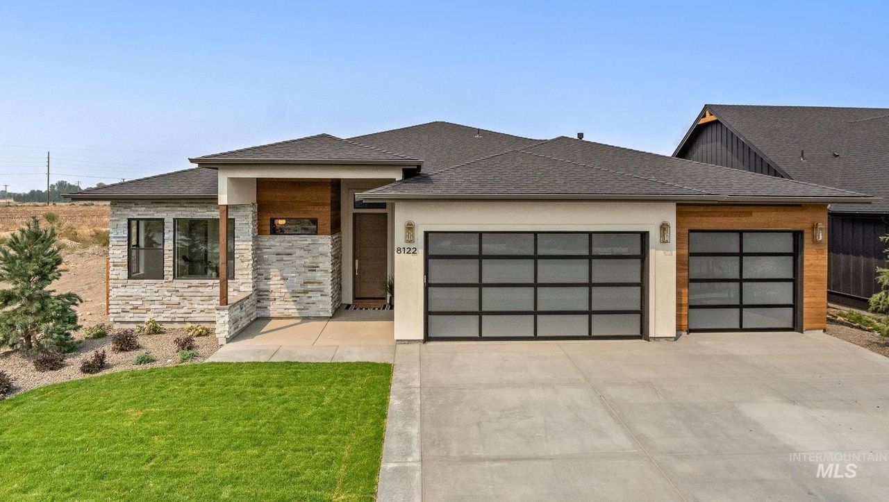 Contemporary house with a gray roof and garage, stone and wood accents, and a concrete driveway.