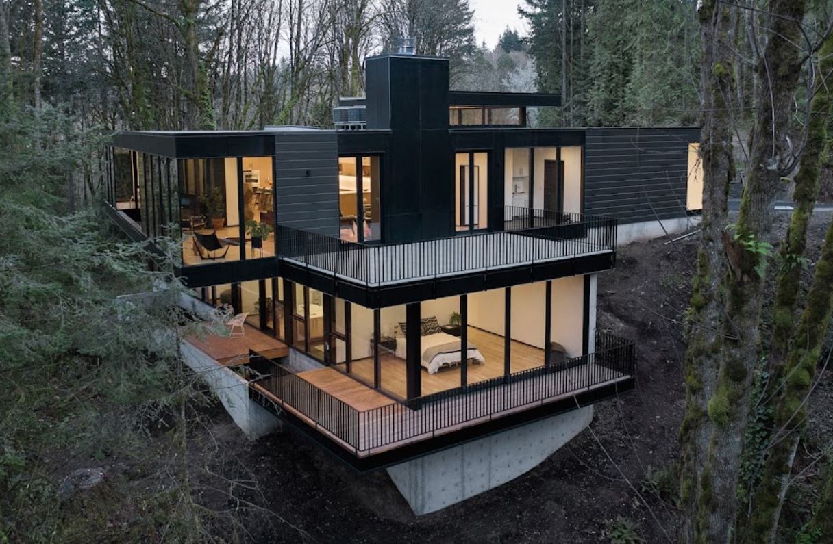 Modern black home with large windows built into a hillside, surrounded by trees.