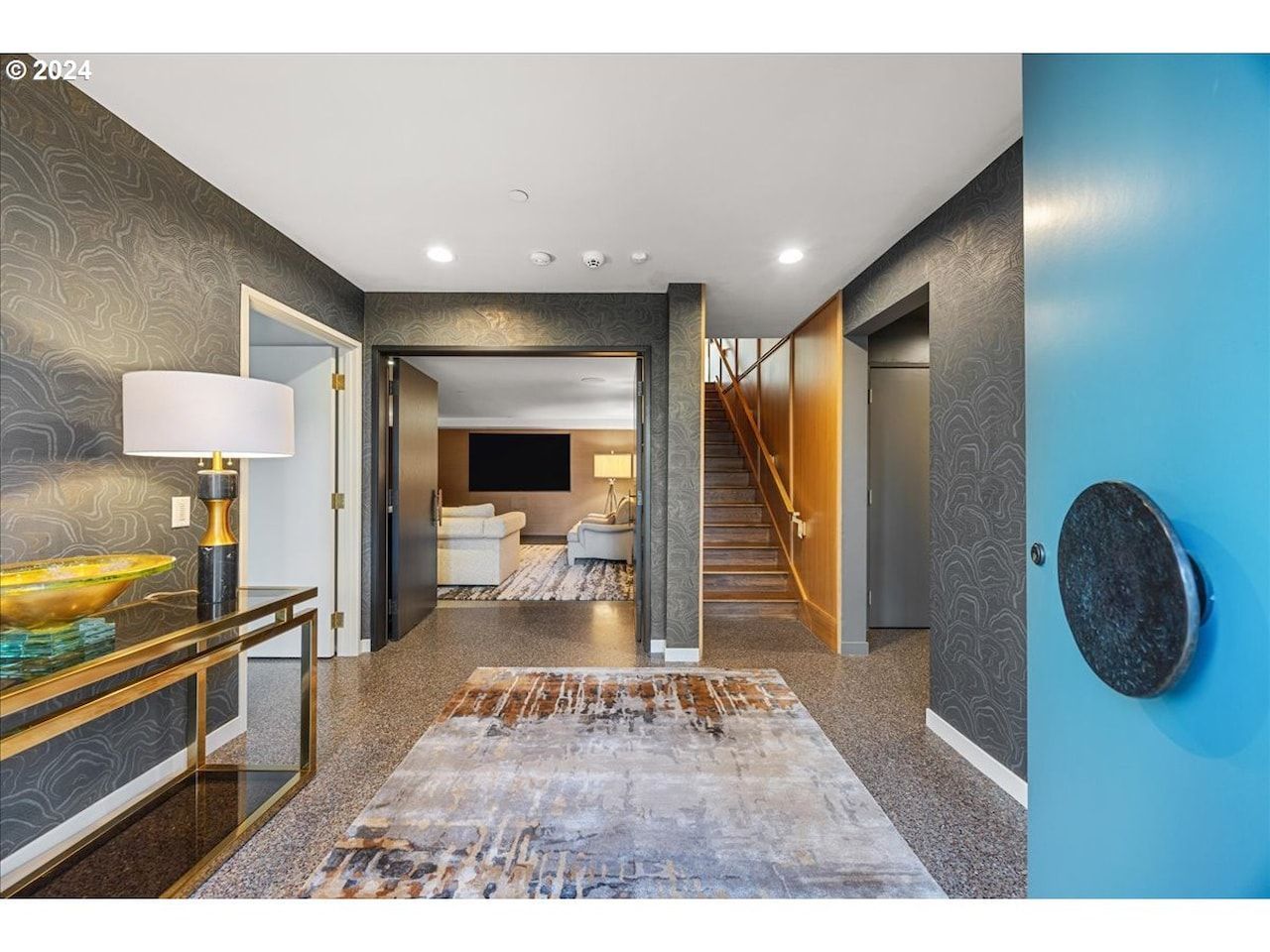 Entryway with teal door, dark textured walls, gold accents, and a staircase leading upwards.