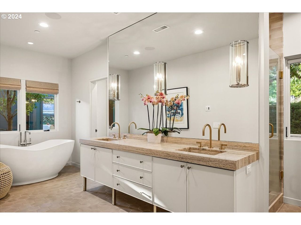 Modern bathroom with white vanity, soaking tub, gold fixtures, and orchid arrangement.