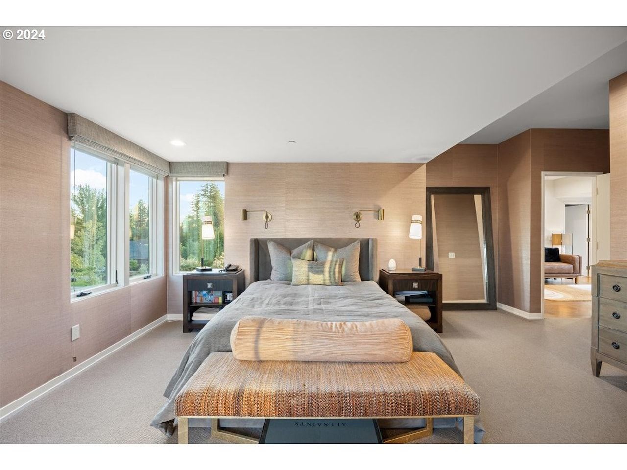 Bedroom with bed, bench, windows, and full-length mirror. Neutral color scheme, natural light.