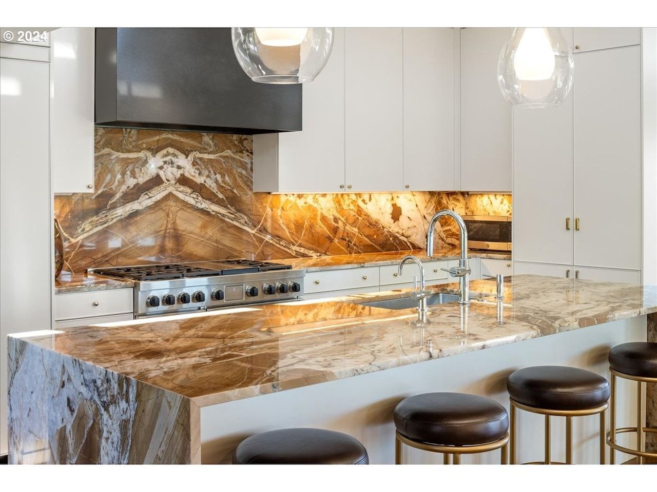 Modern kitchen with marble countertops, brown backsplash, and pendant lights.