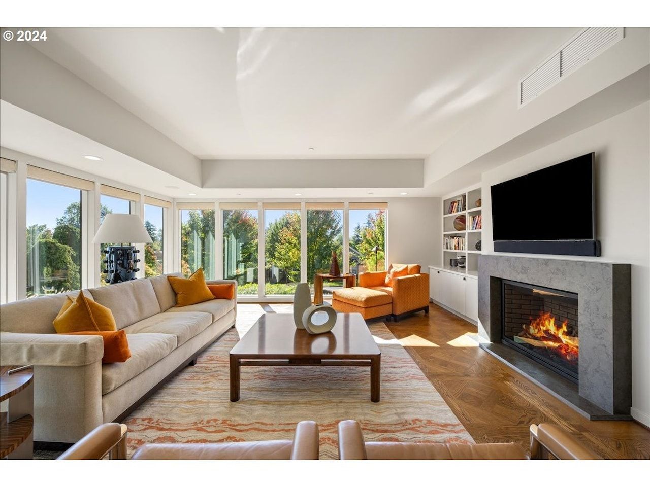 Living room with fireplace, windows, neutral sofa, orange chair, and area rug.