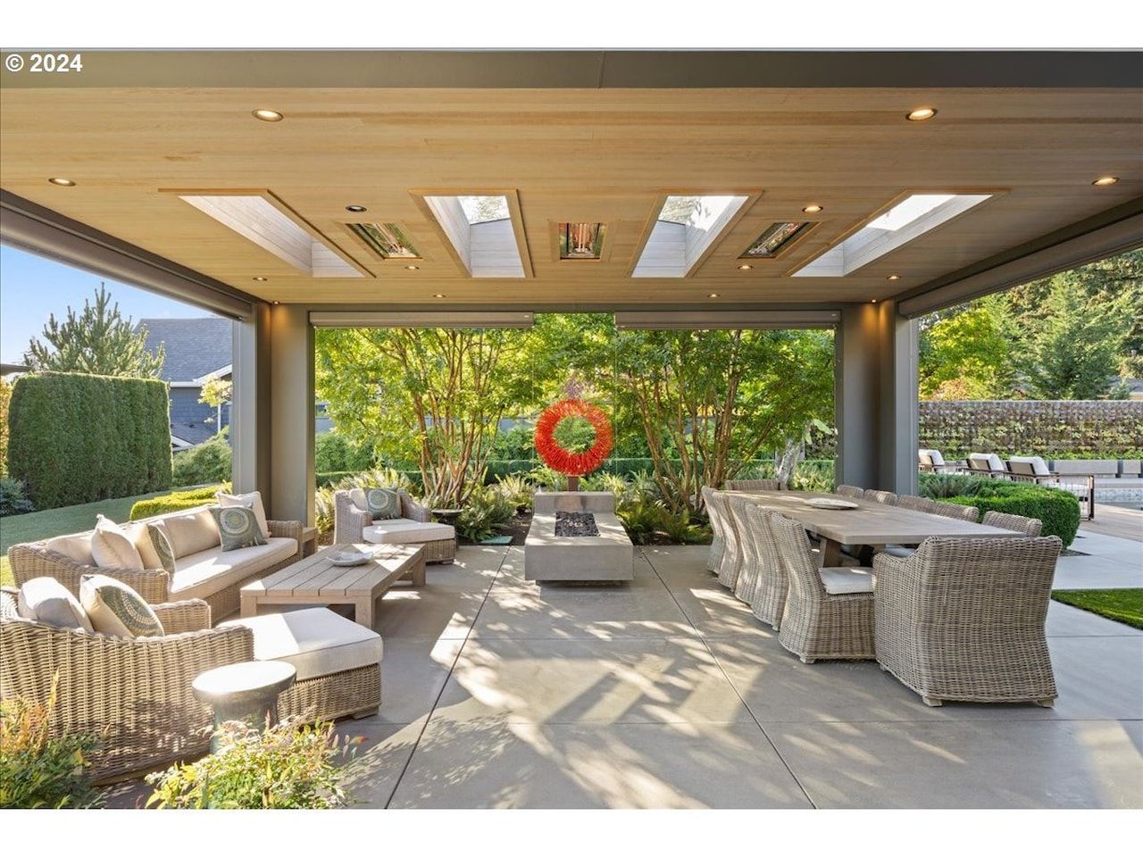 Covered patio with wicker furniture and a dining table, overlooking a backyard.