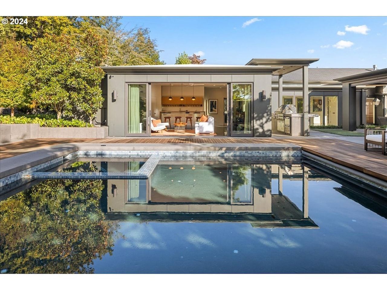 Modern home with pool; open doors reveal interior. Reflection in water, blue sky.