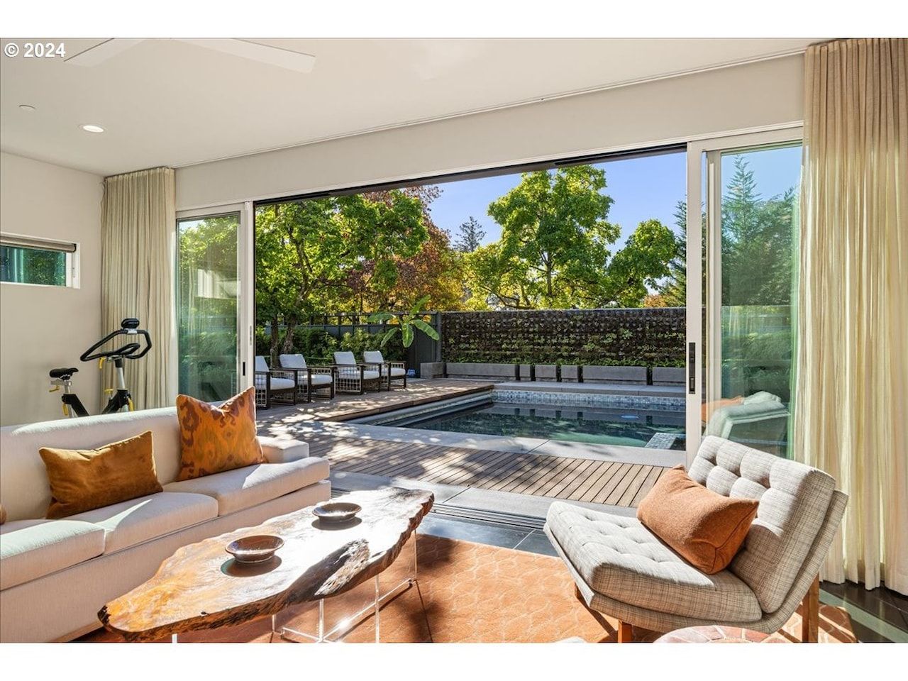 Living room with open sliding doors to a pool and backyard; white and orange accents.