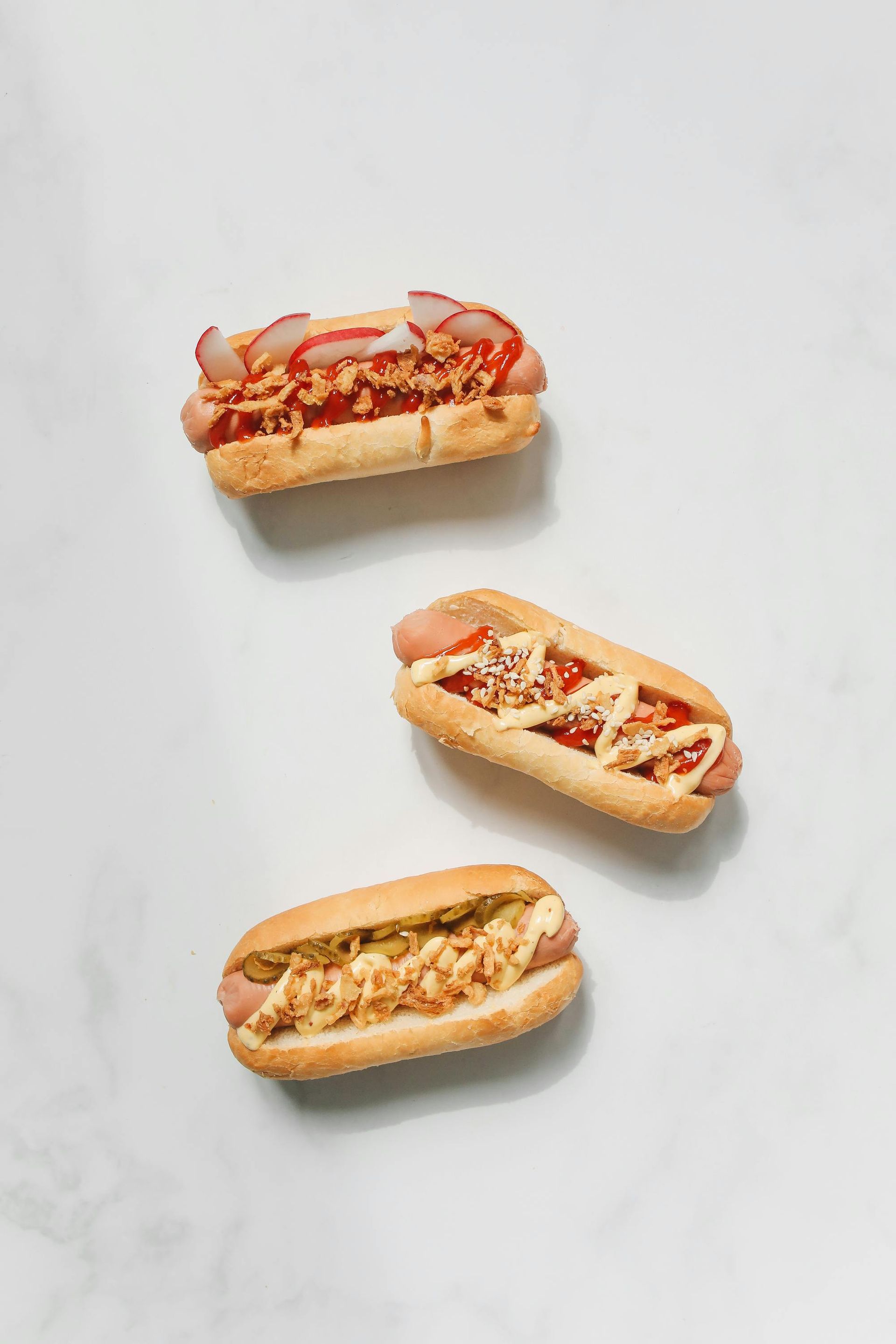 Three hot dogs with different toppings on a white surface.
