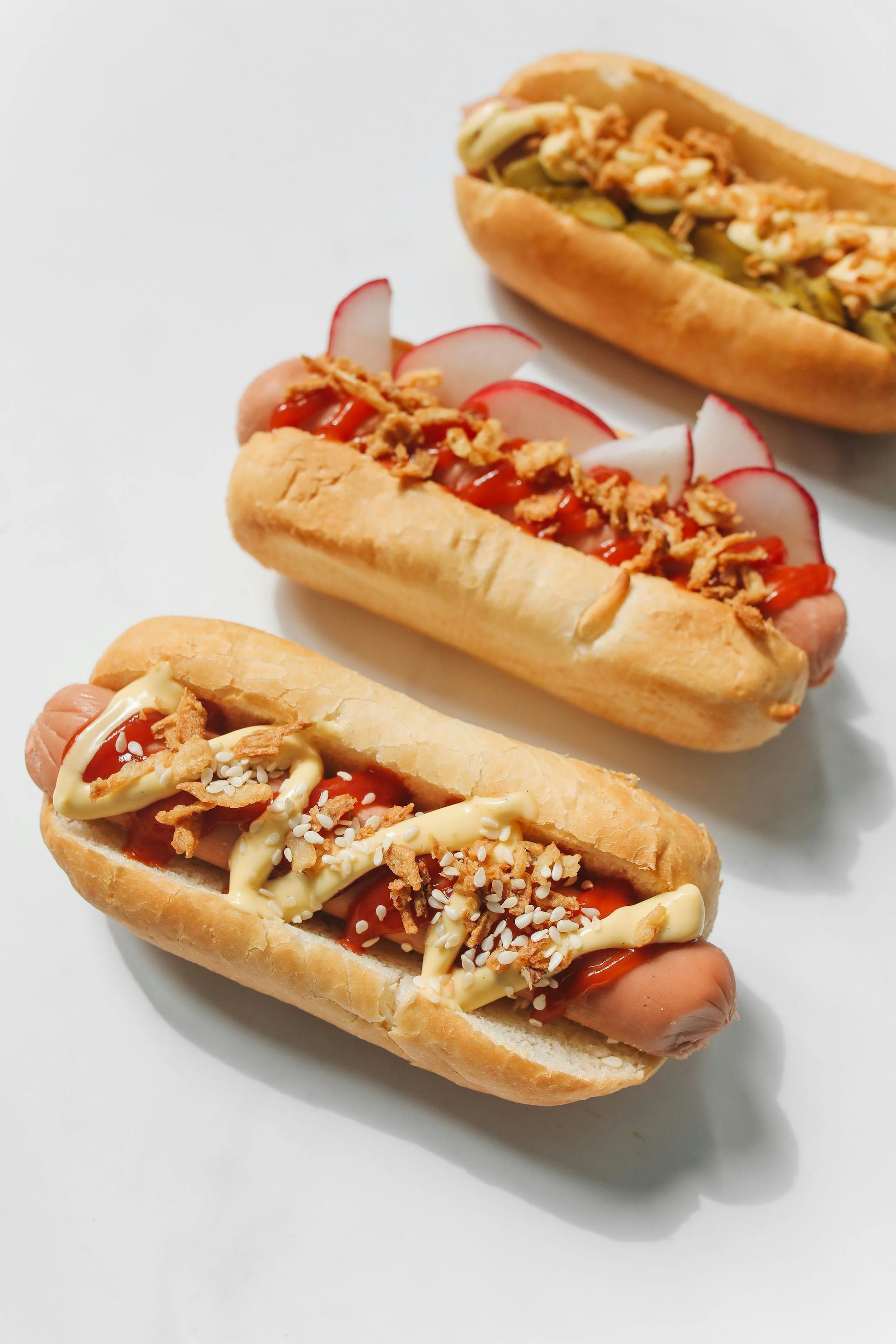 Three hot dogs with different toppings on a white surface.