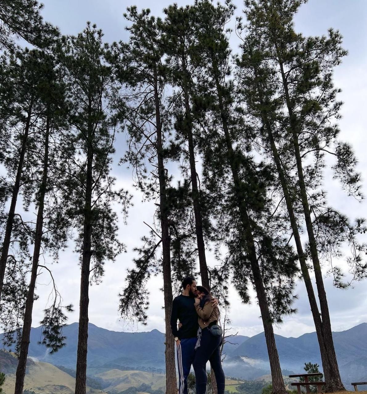 Um casal em pé sob uma árvore com montanhas ao fundo