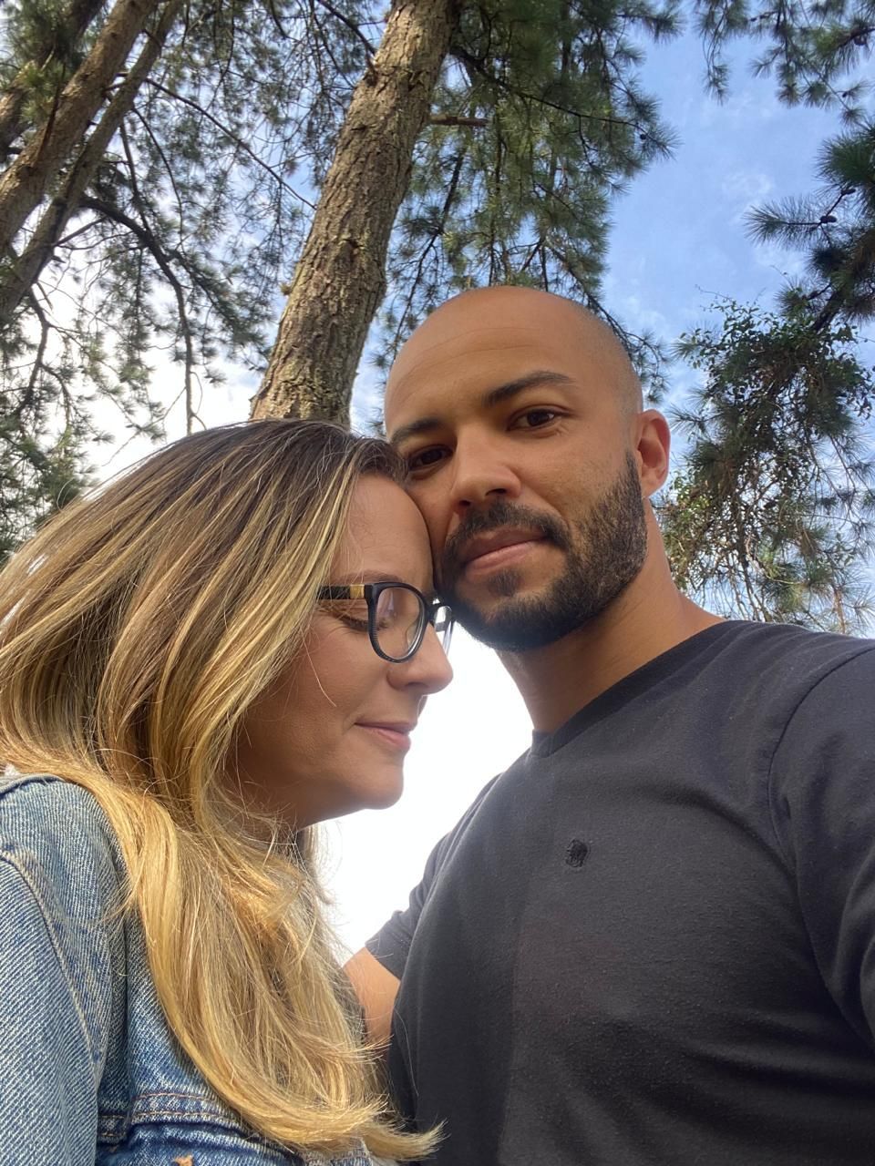 Um homem e uma mulher estão parados um ao lado do outro em frente a uma árvore.