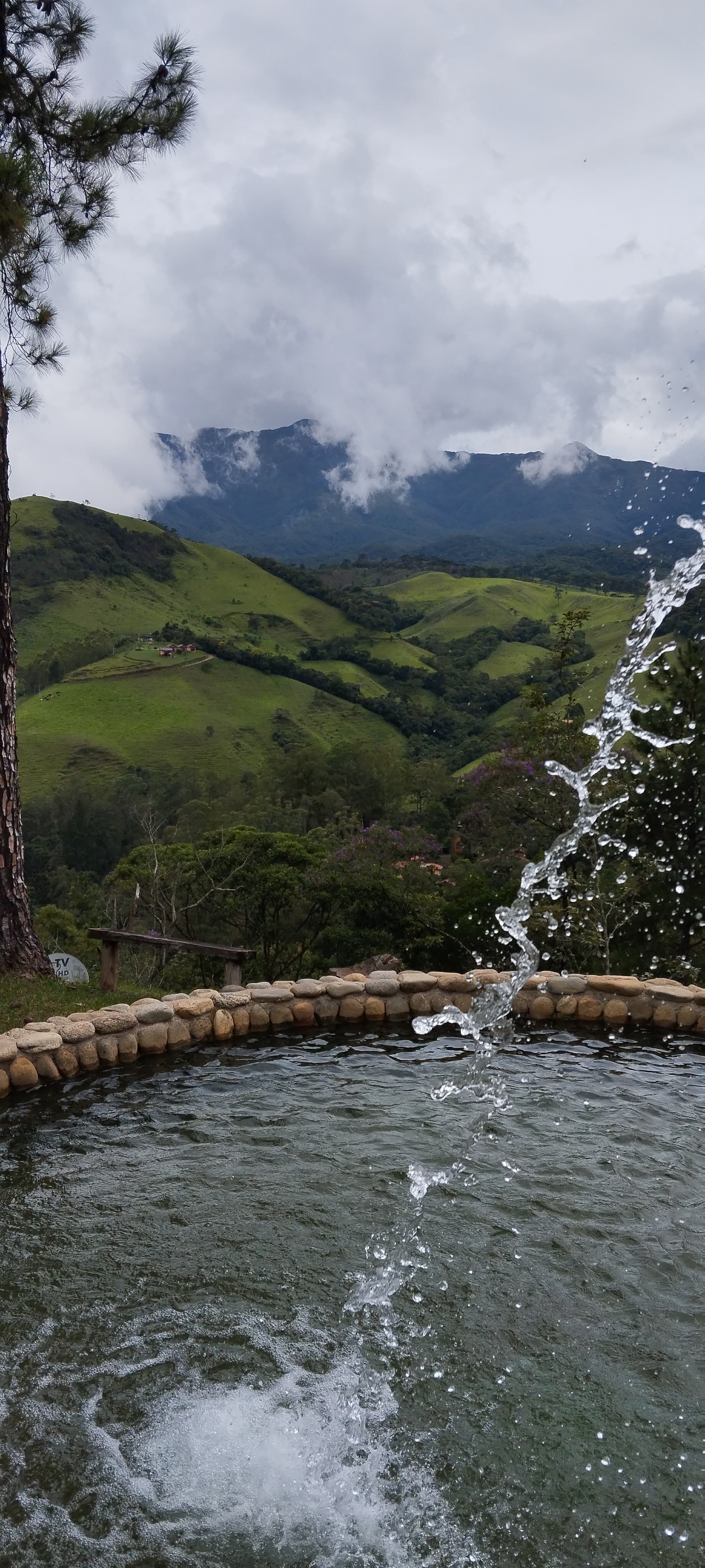 Um lago com uma cachoeira ao fundo e montanhas ao fundo.