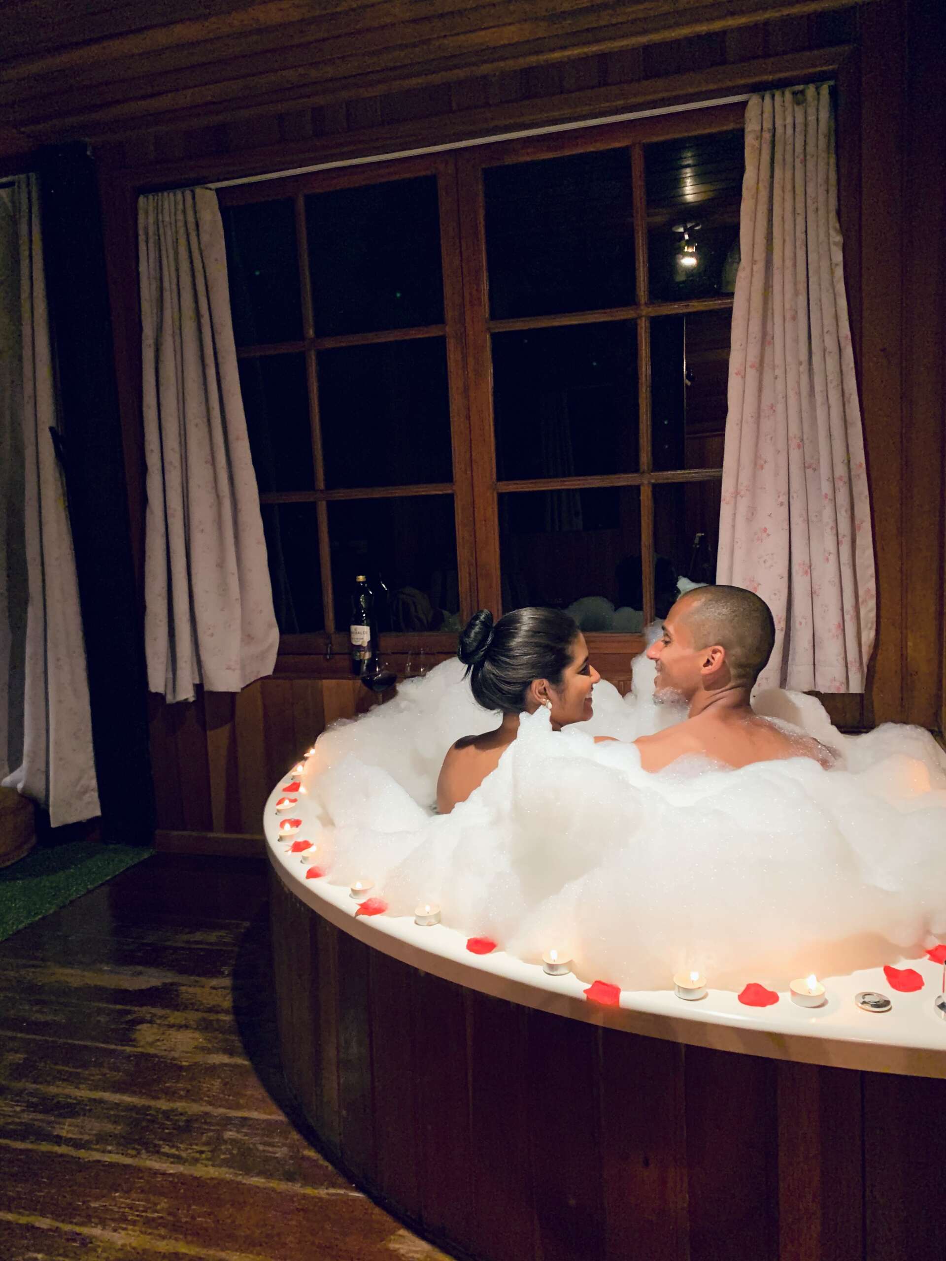 Um homem e uma mulher estão tomando um banho de espuma em uma banheira redonda.