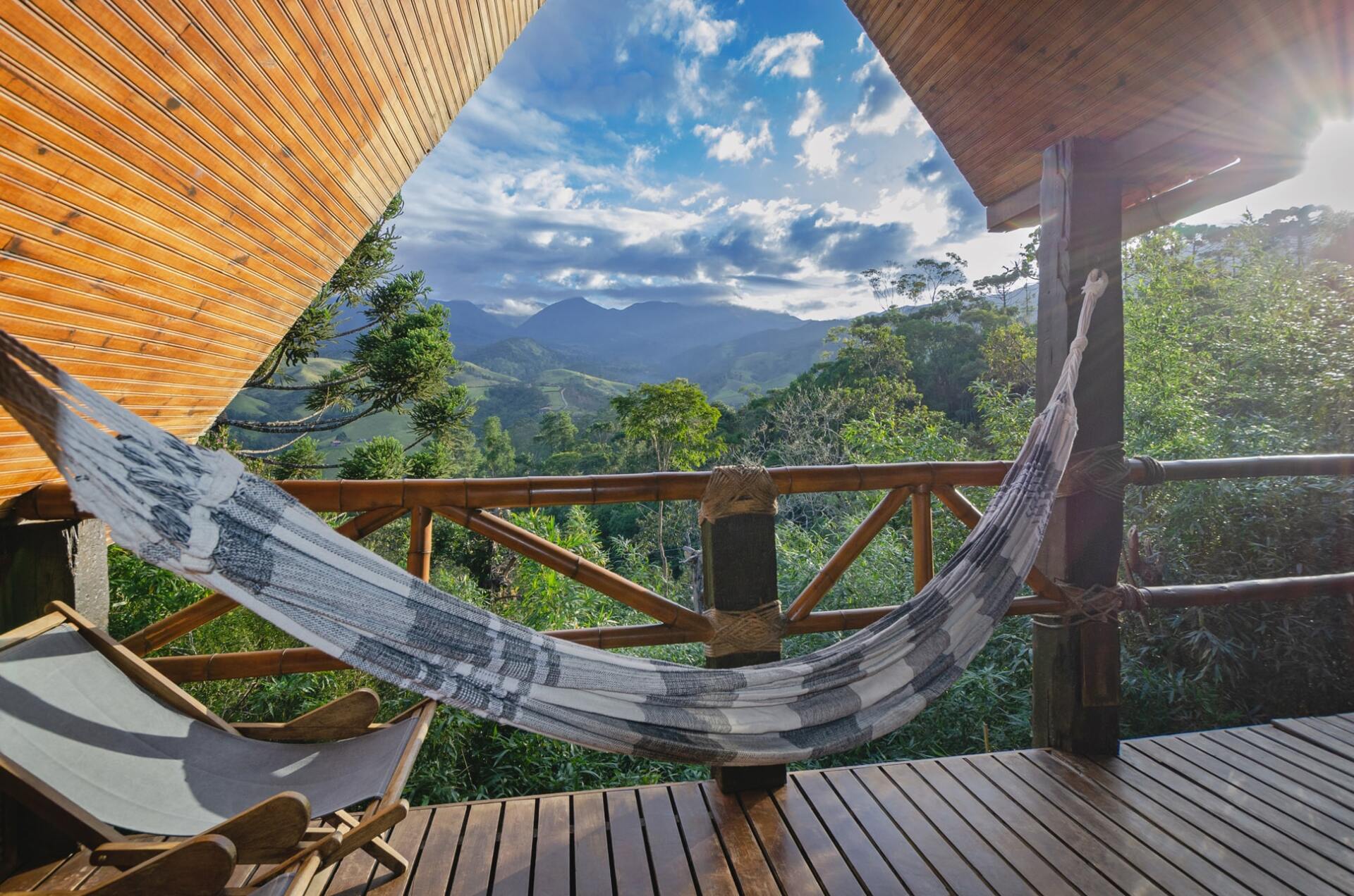 Uma rede está pendurada em um deck de madeira com vista para uma floresta.