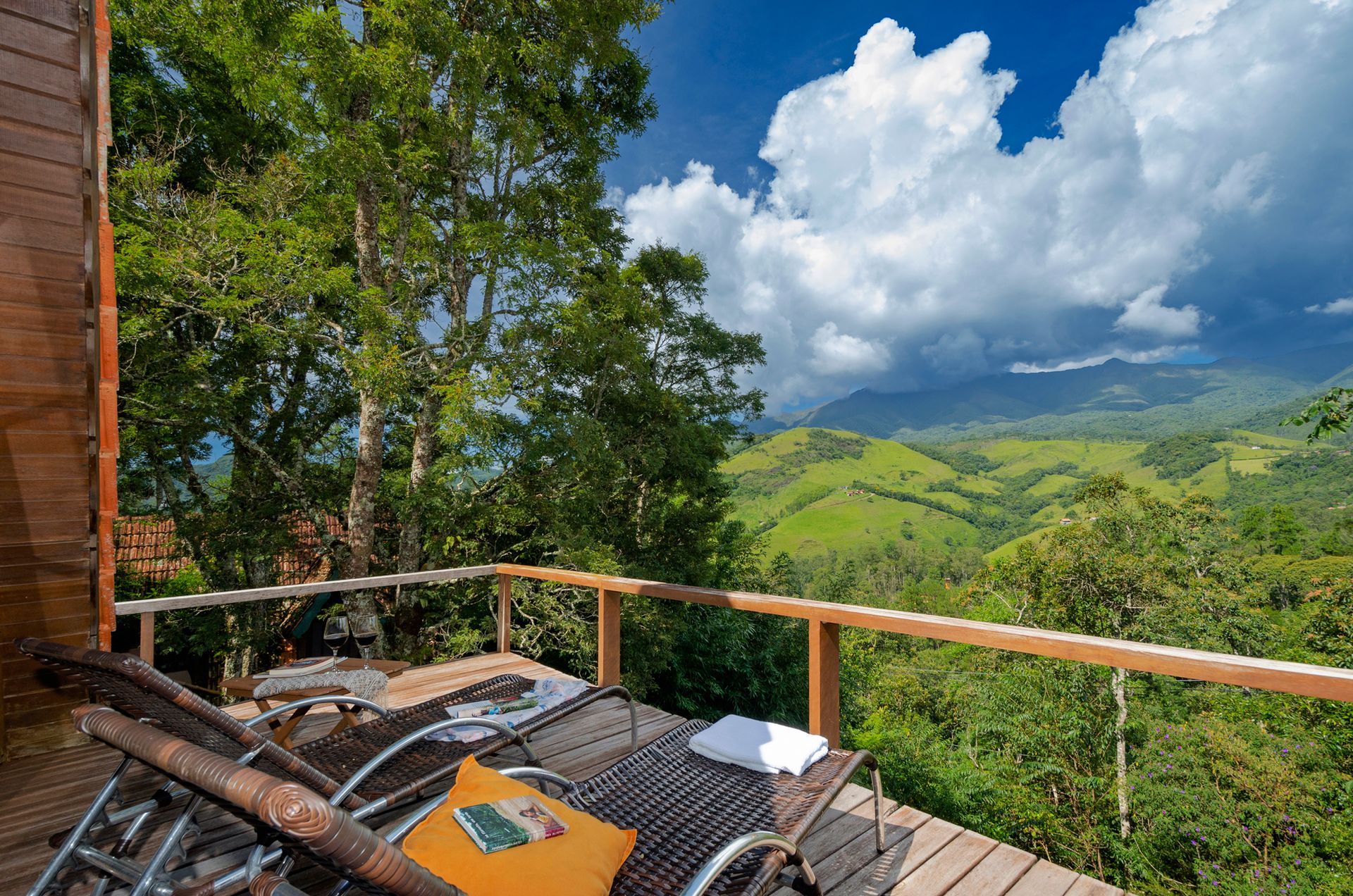 Duas espreguiçadeiras estão sobre um deck de madeira com vista para uma floresta verdejante.