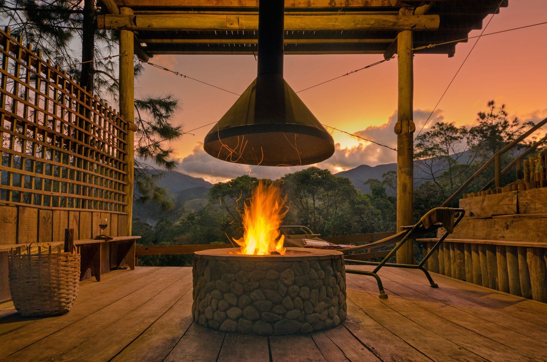 Uma fogueira em um deck de madeira com um pôr do sol ao fundo.
