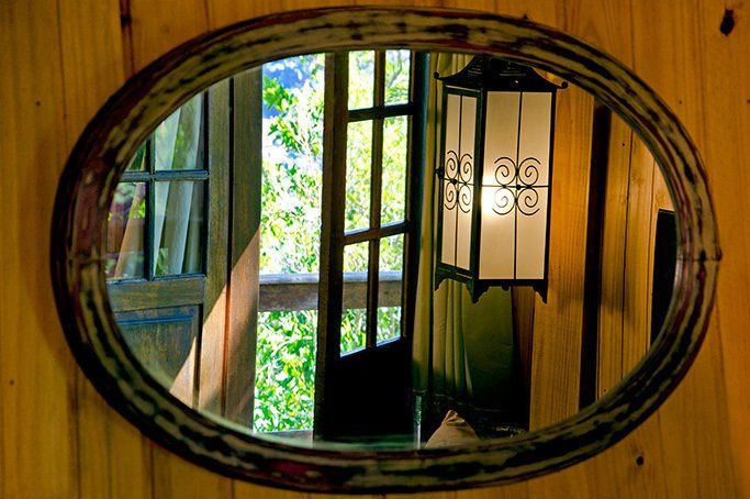 Um espelho em uma parede de madeira mostra uma janela e uma lâmpada