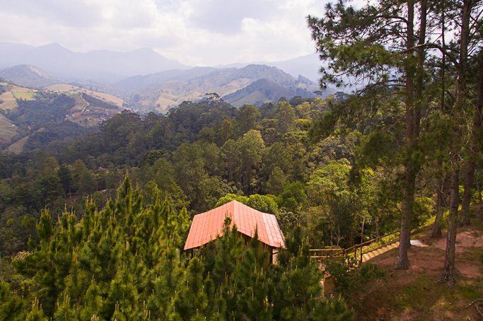 Uma vista aérea de uma casa no meio de uma floresta com montanhas ao fundo.