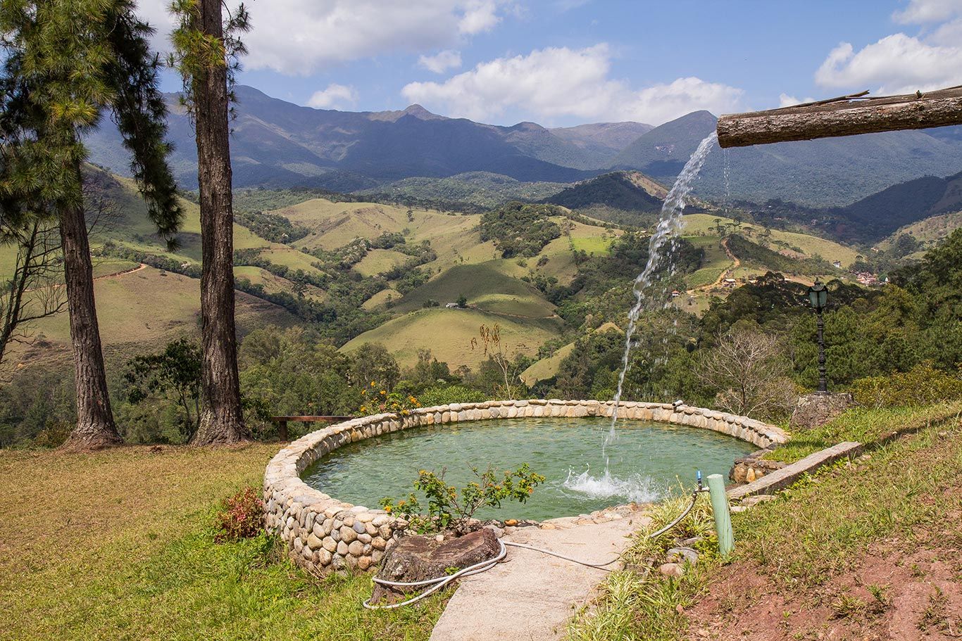 Uma fonte jorra água em um lago com montanhas ao fundo.