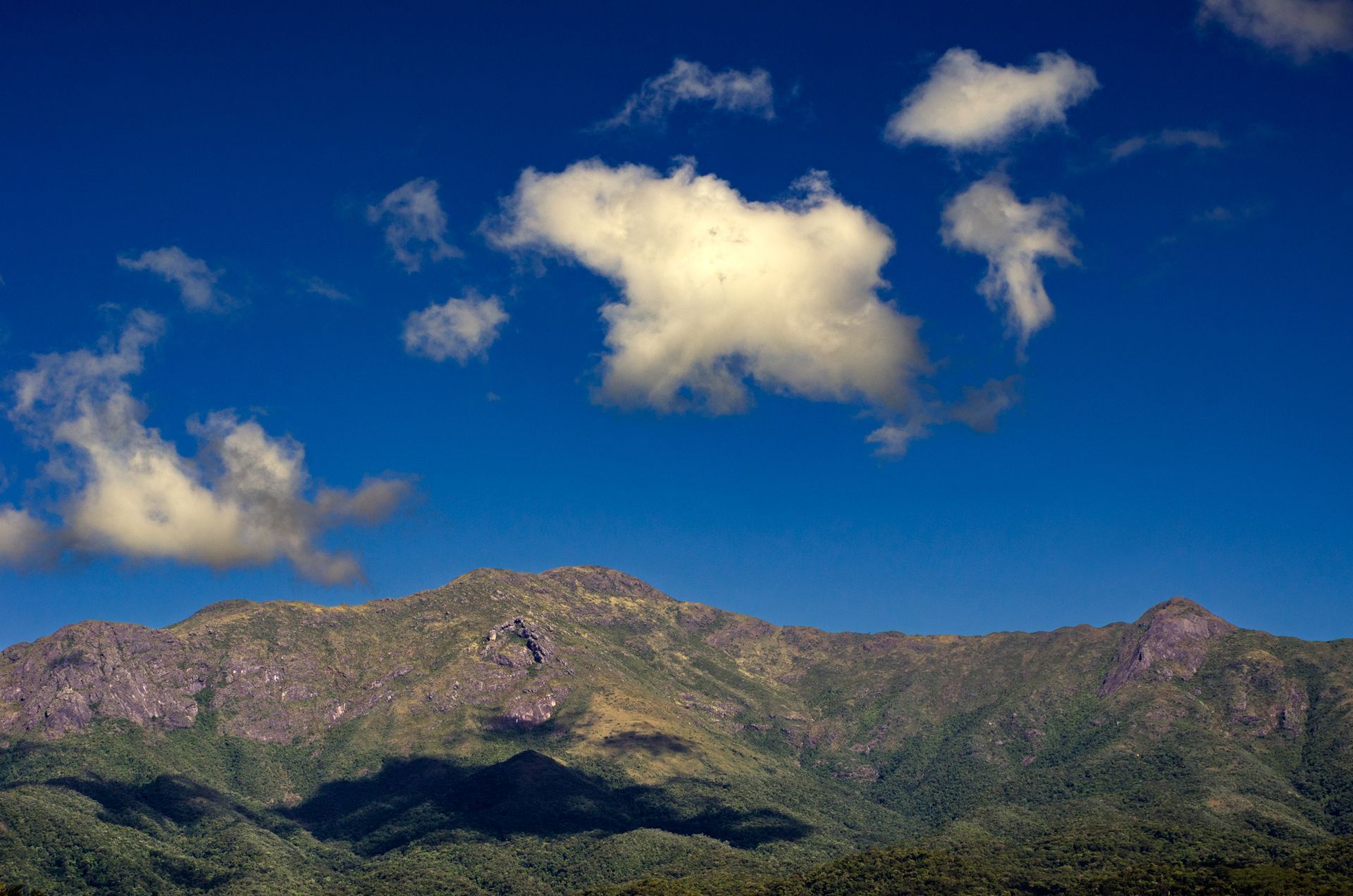 Uma cadeia de montanhas com um céu azul e nuvens ao fundo.