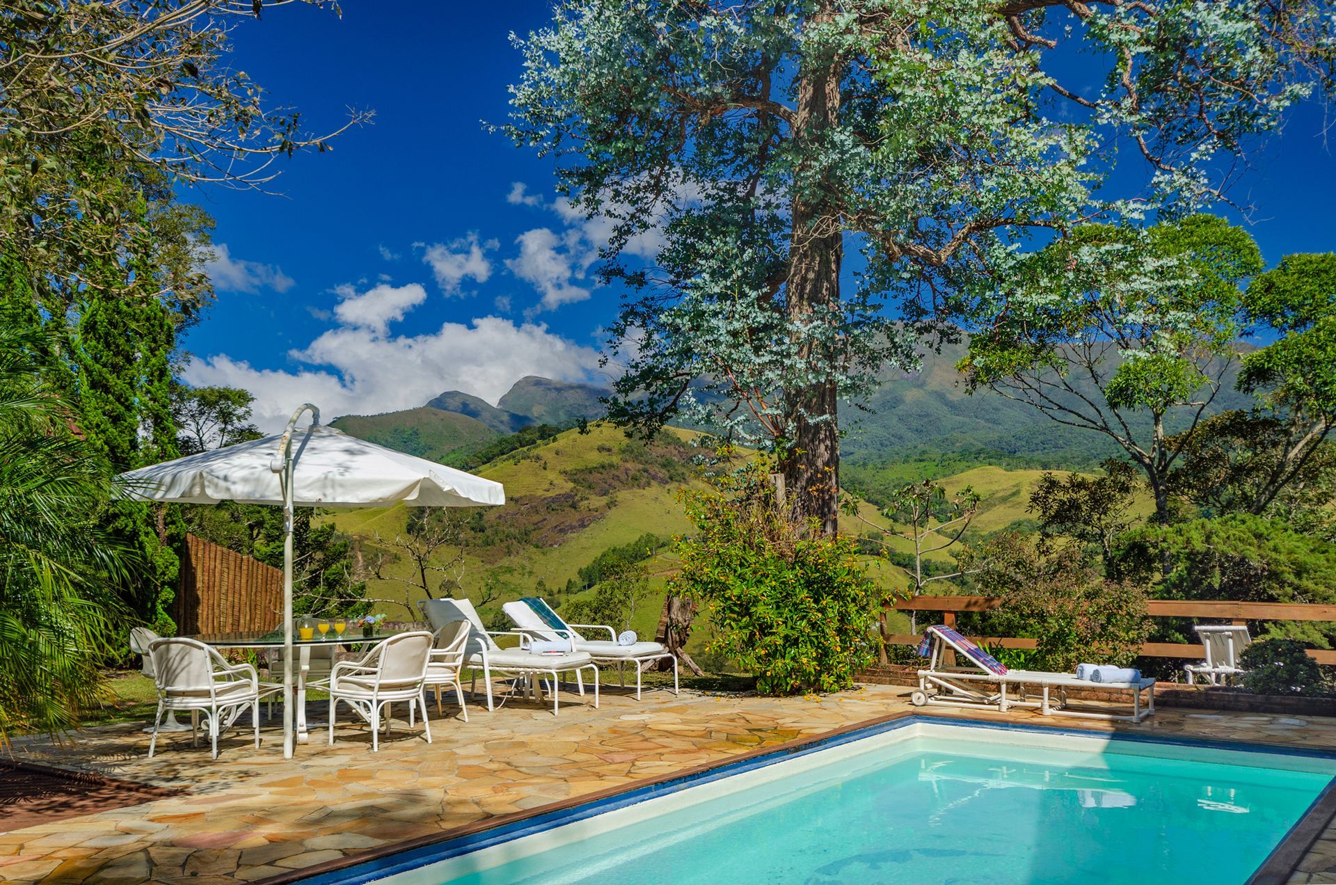 Uma piscina cercada por cadeiras e guarda-sóis com montanhas ao fundo.