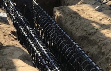 A bunch of black pipes are laying in the dirt.