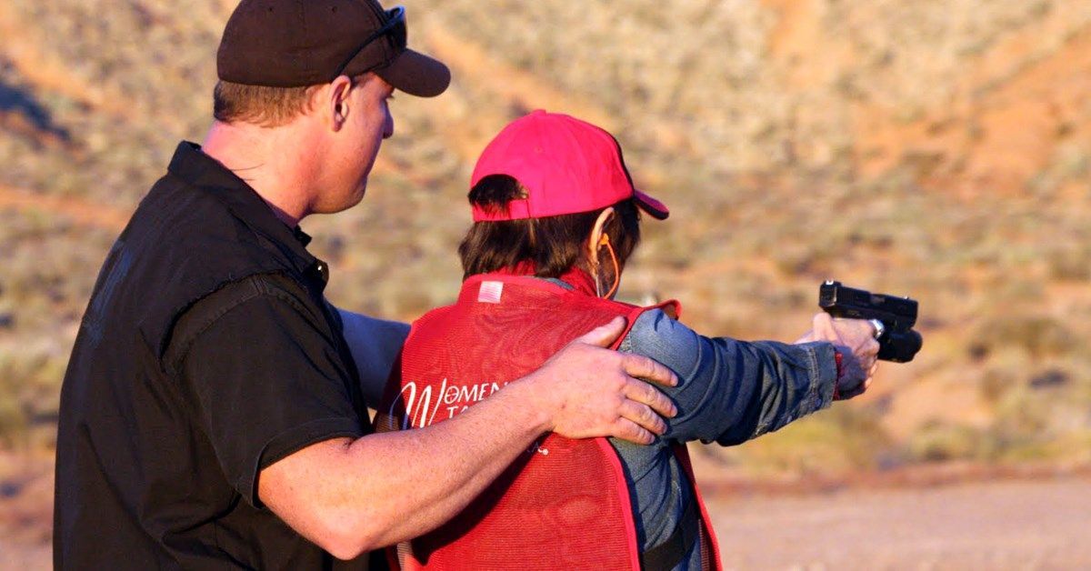 Instructor assists woman with pistol at outdoor shooting range.