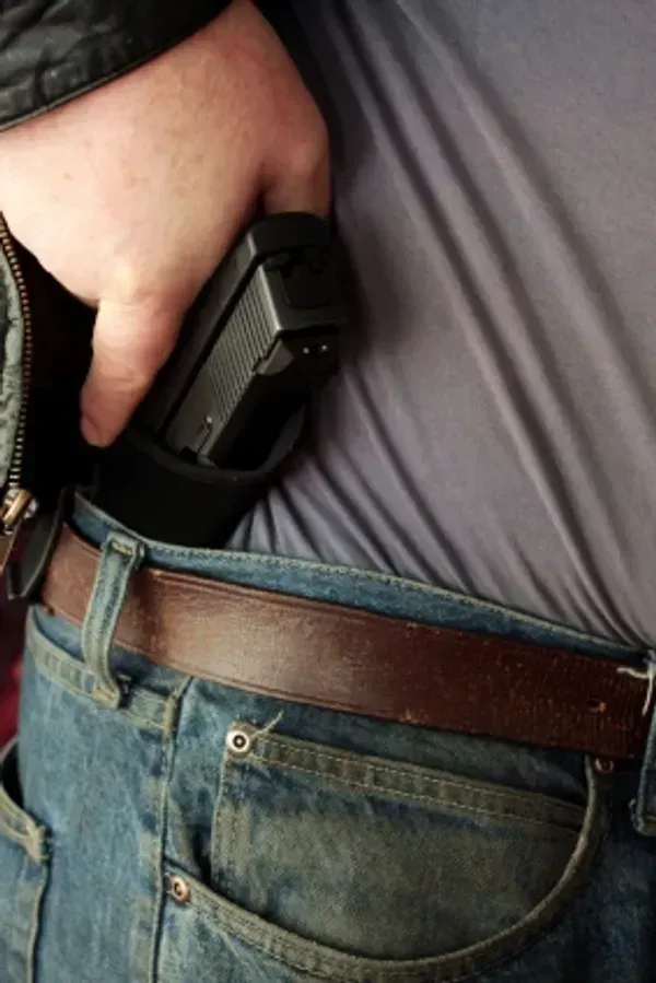 Man drawing a black handgun from a holster inside his jeans, brown belt visible.