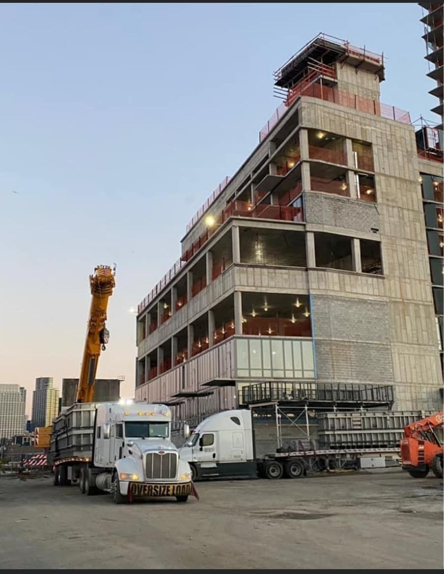 Trucks at a construction site; a large building under construction, crane, cement trucks and sky.