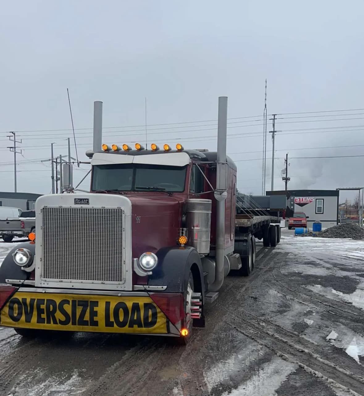 A maroon Peterbilt truck hauls an oversized load.  The truck is labeled 