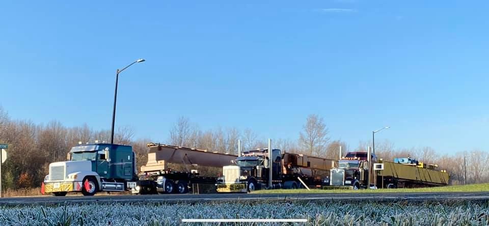 A semi truck is parked in a parking lot with containers in the background.