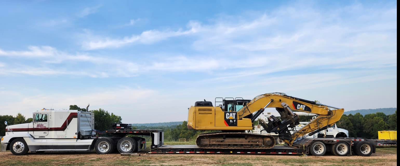 A yellow excavator is on the back of a semi truck.