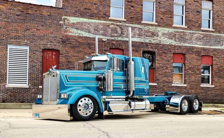 A blue semi truck is parked in front of a brick building.