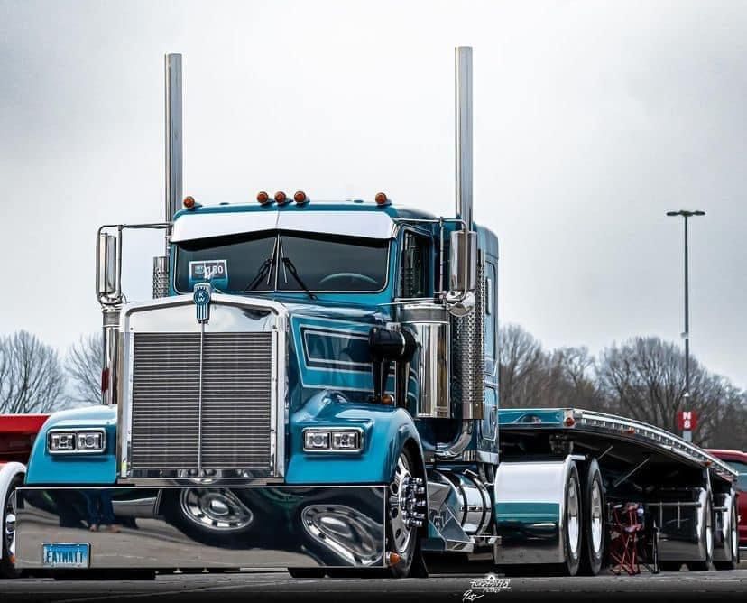 A blue semi truck with a flatbed trailer is parked on the side of the road.