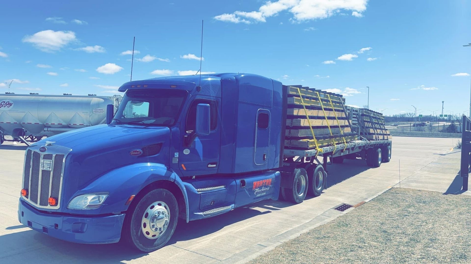 Blue semi-truck loaded with metal sheets parked outdoors on a sunny day.