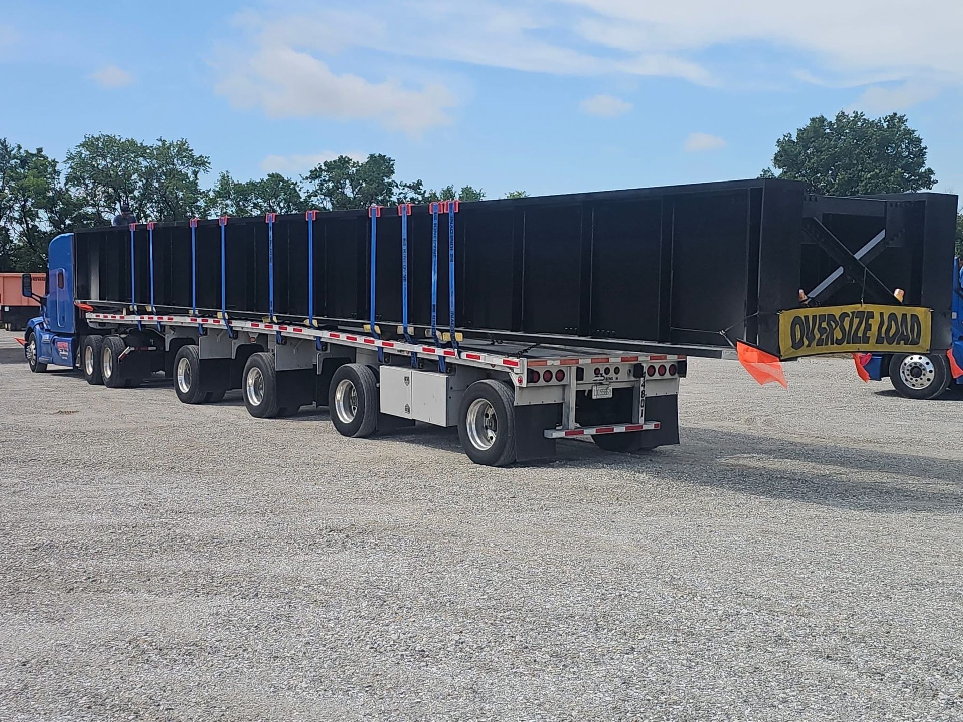 A long, black oversized load being transported on multiple flatbed trailers under a blue sky.