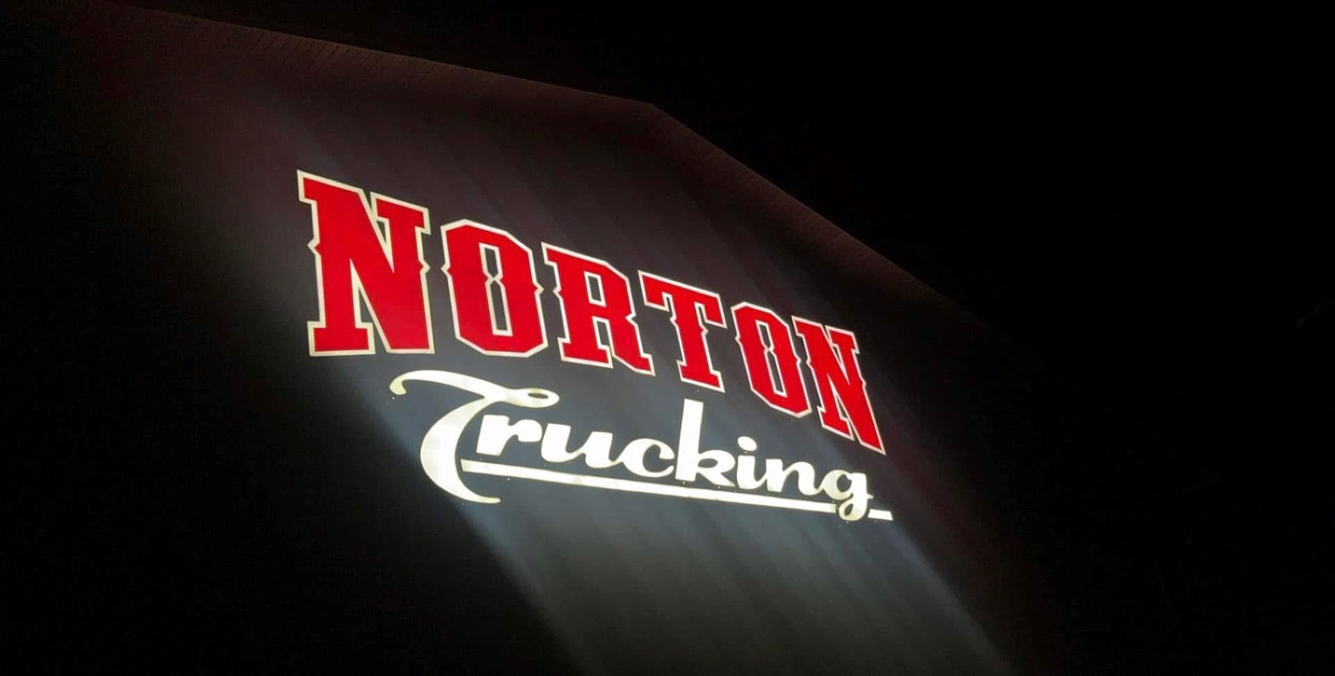 A norton trucking sign is lit up at night